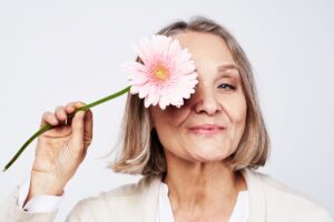 menopausal woman holding a pink flower in from of face 